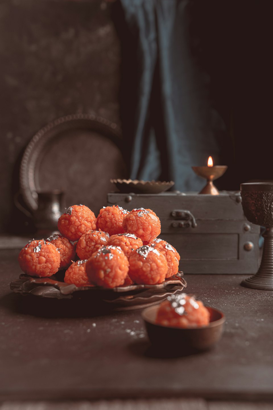 Orange ladoo sweets with silver leaf on an ornate plate.
