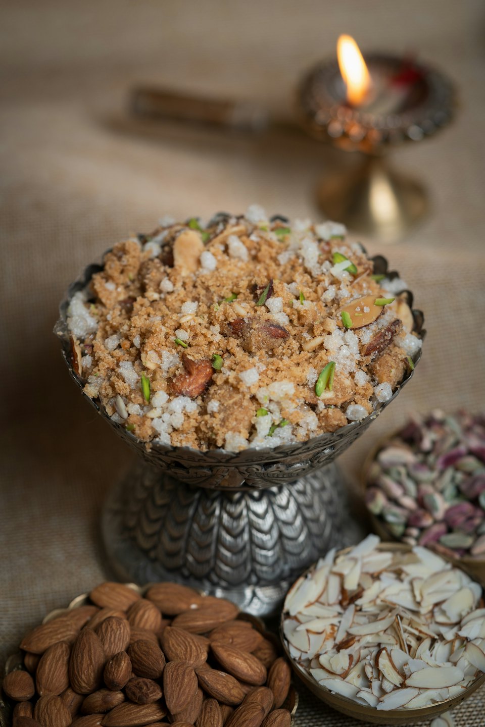 A silver bowl of garnished Indian dessert sits beside nuts.