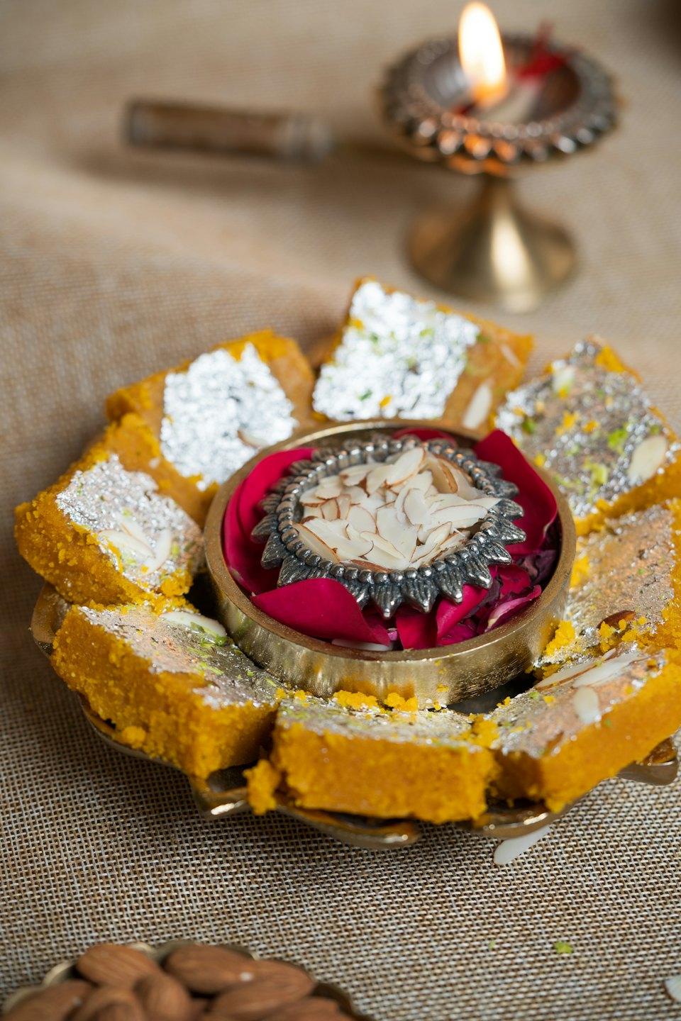 Indian sweets topped with silver leaf arranged around rose petals.